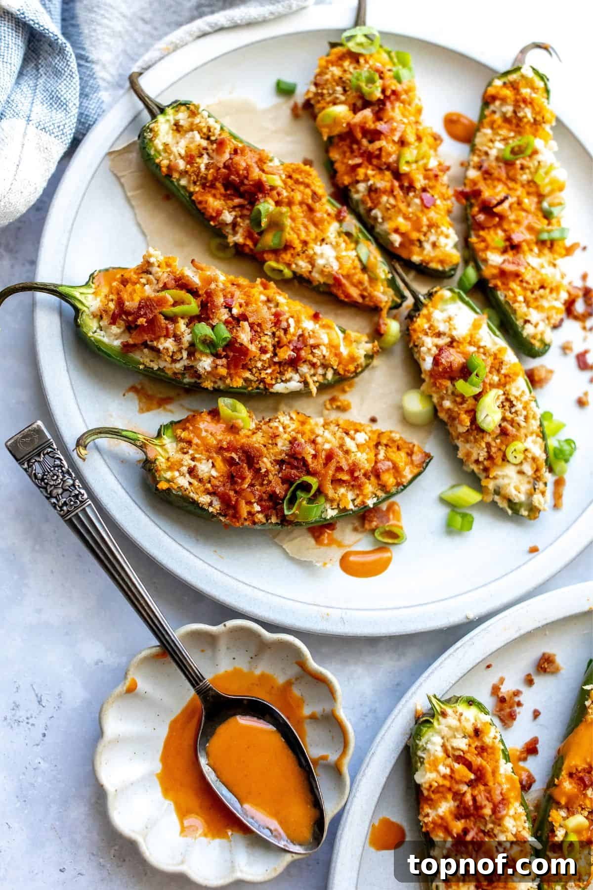 A close-up of beautifully golden-brown Oven Baked Jalapeño Poppers on a plate, garnished with fresh chives, with a serving spoon nearby. The creamy filling is visible, inviting a taste.