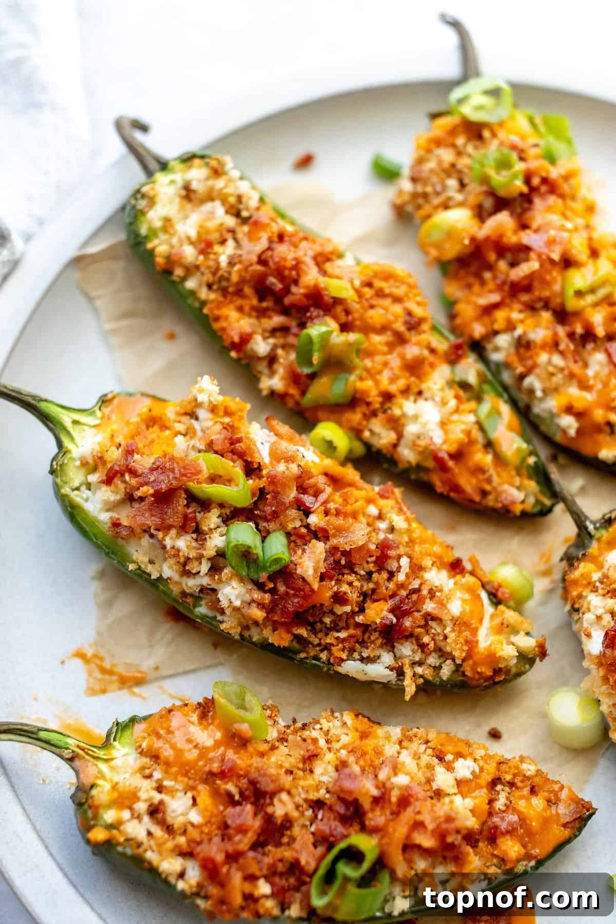 A stunning close-up, overhead shot of the finished Oven Baked Jalapeño Poppers on a serving plate, exquisitely garnished with fresh chives and crispy bacon, highlighting their inviting appeal.