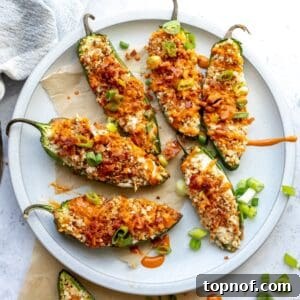 Close-up, overhead shot of baked jalapeño poppers on a plate, garnished with chives and bacon, showcasing their delicious appeal.