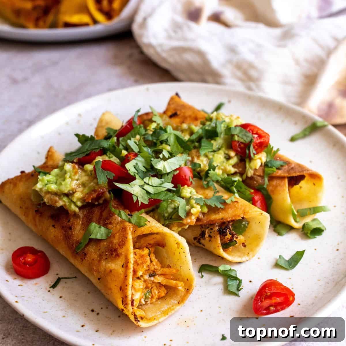 Golden Crisp Chicken Taquitos 2 Crispy baked chicken taquitos on a wire rack, ready to be served, with a vibrant garnish of fresh cilantro and a dollop of sour cream visible in the background, hinting at delicious toppings.