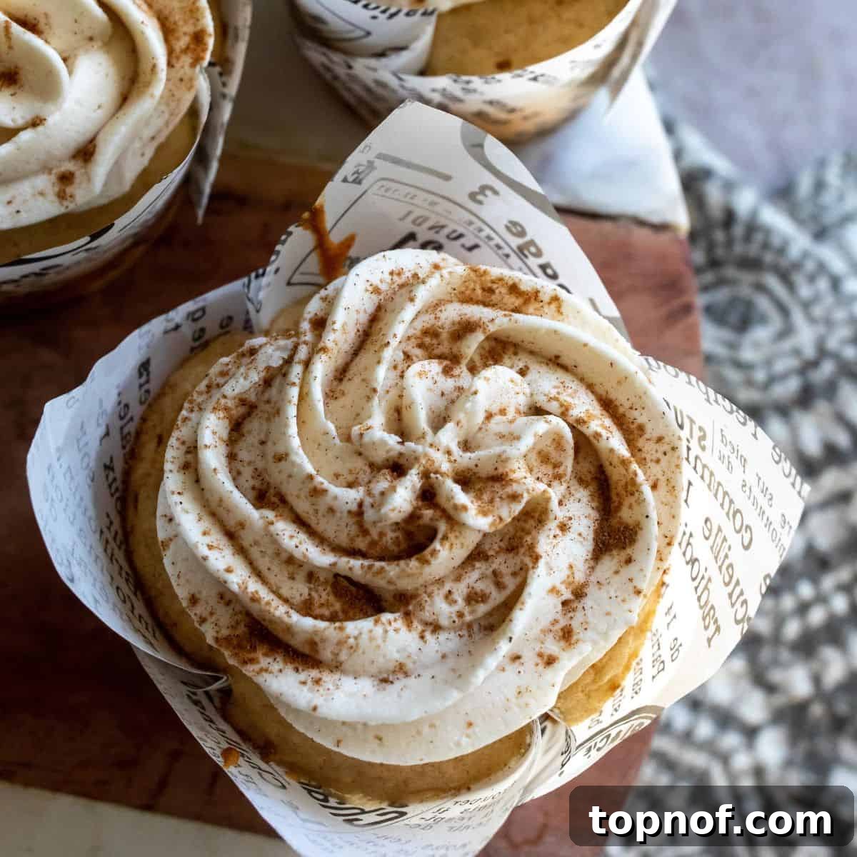 A single Apple Cider Cupcake up close, perfectly baked in its wrapper with a hint of frosting and a sprinkle of spice.