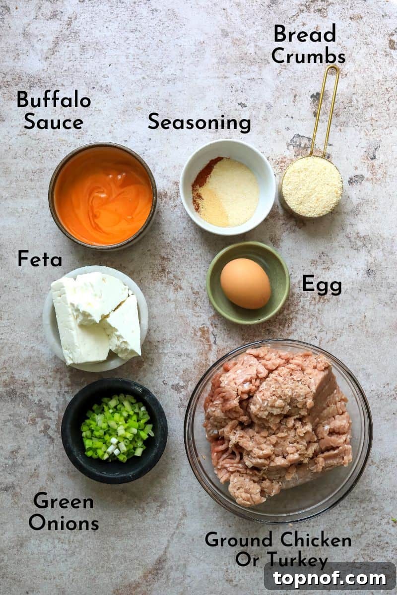 A selection of fresh ingredients laid out on a kitchen counter, including ground chicken, buffalo sauce, breadcrumbs, feta cheese, an egg, and various spices, all ready for preparing buffalo chicken meatballs.