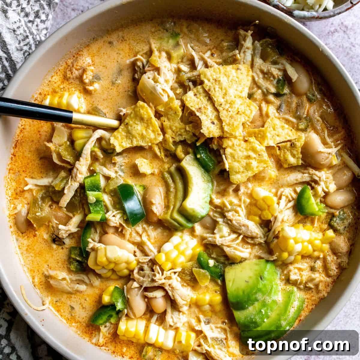 Creamy Chicken White Bean Chili 2 A steaming bowl of White Bean Chicken Chili topped with fresh avocado slices and crispy tortilla chips, ready to be enjoyed.
