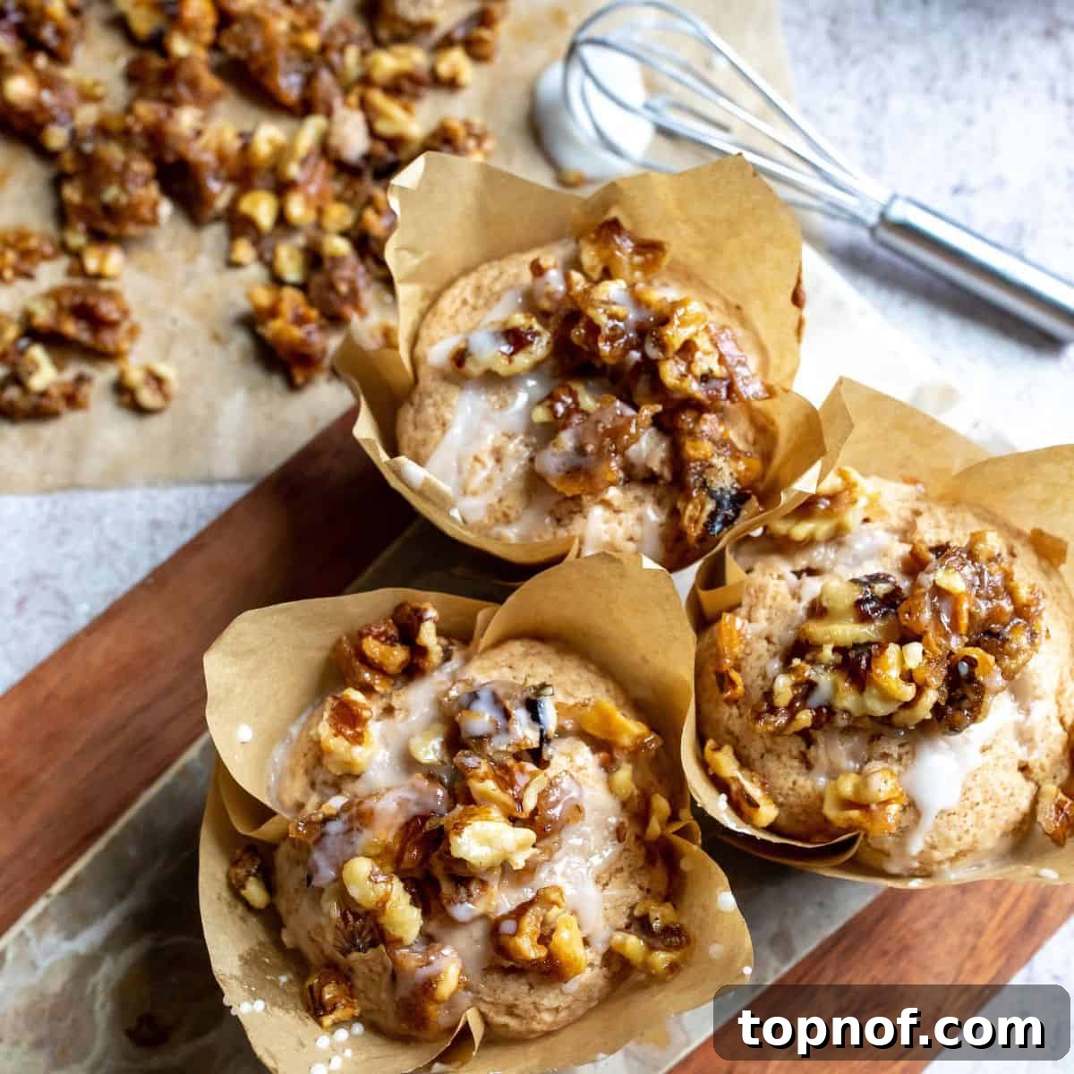 Bakery Style Cinnamon Muffins with Candied Walnuts 2 Warm cinnamon muffins elegantly arranged on a rustic wooden cutting board, showcasing their golden-brown tops and candied walnut garnish.