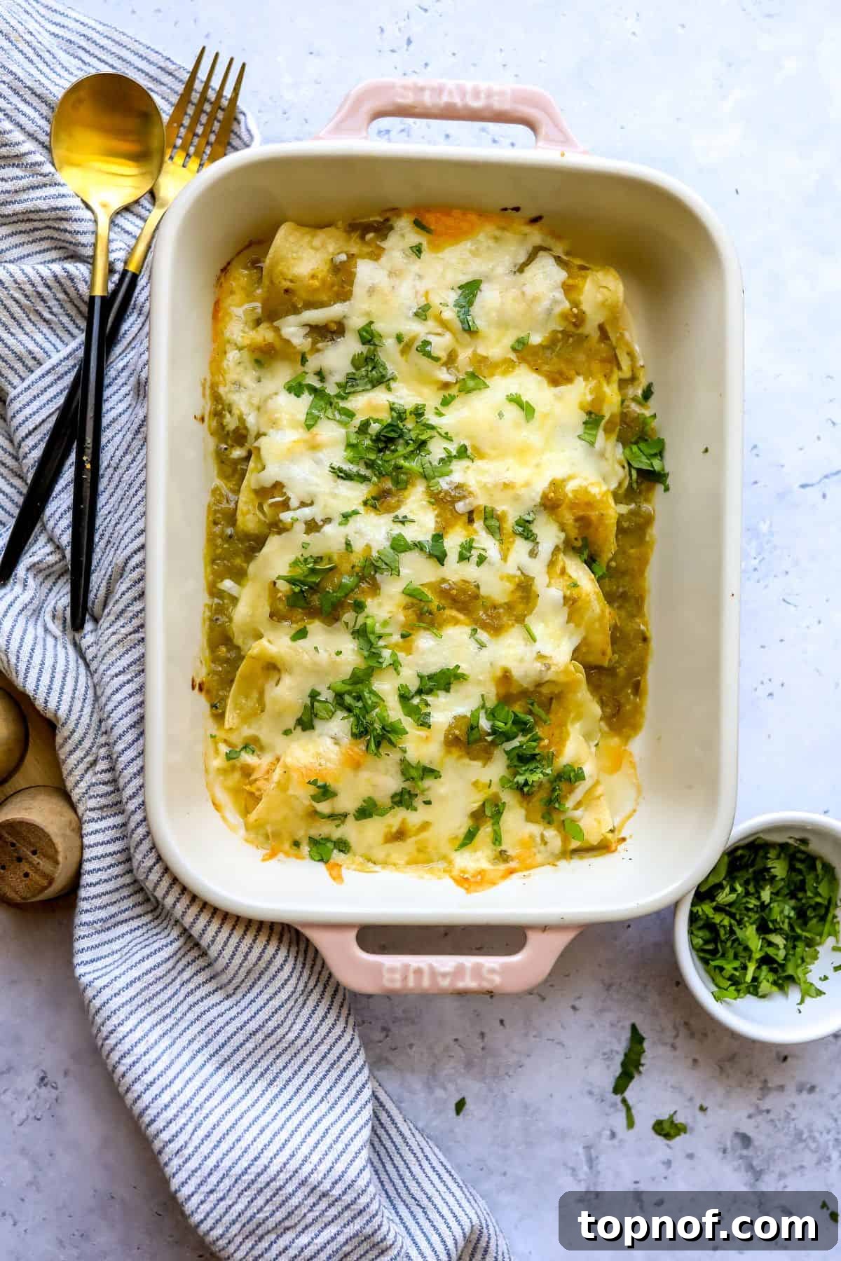 Zesty Green Chile Chicken Enchiladas 2 A beautifully baked dish of Green Chili Chicken Enchiladas, garnished with fresh cilantro, served in a light pink casserole dish.