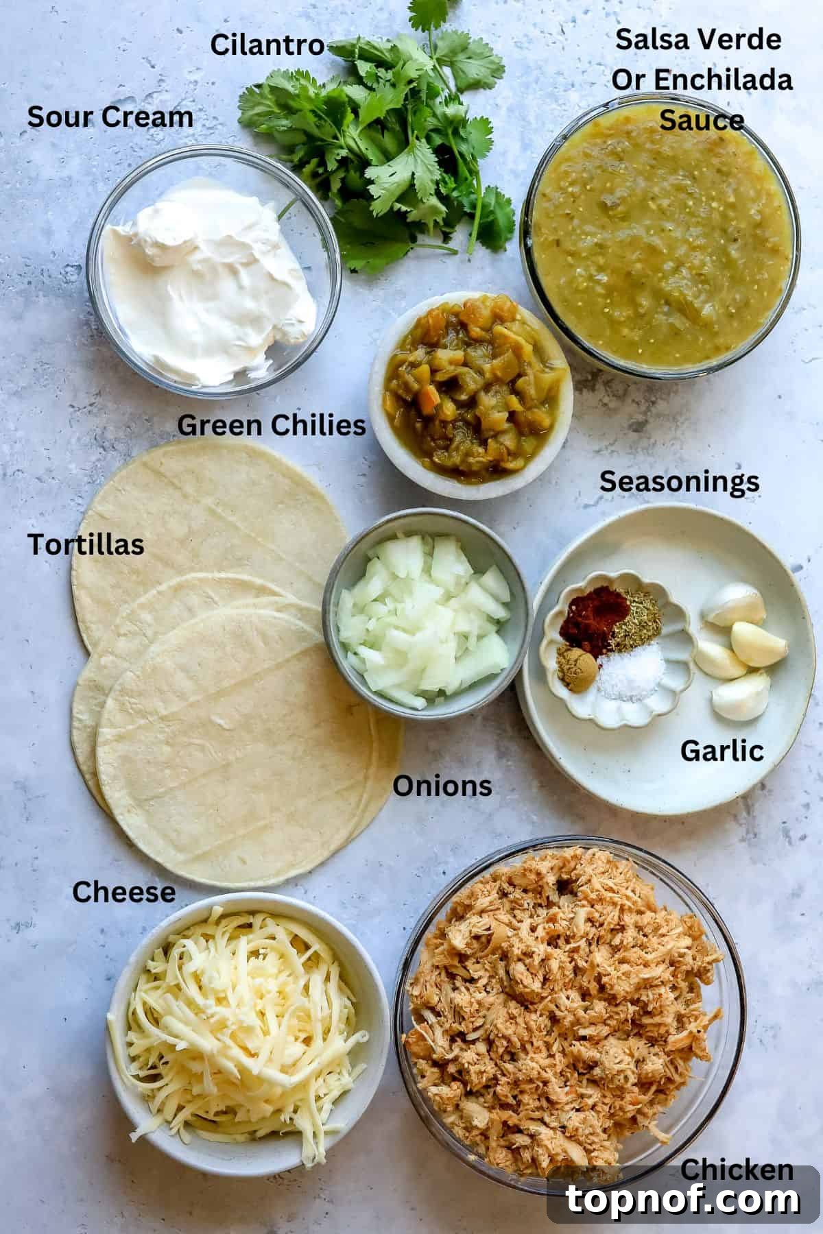 Zesty Green Chile Chicken Enchiladas 3 A collection of fresh ingredients for Green Chili Chicken Enchiladas laid out on a kitchen counter in various bowls, including chicken, cheese, salsa verde, and spices.