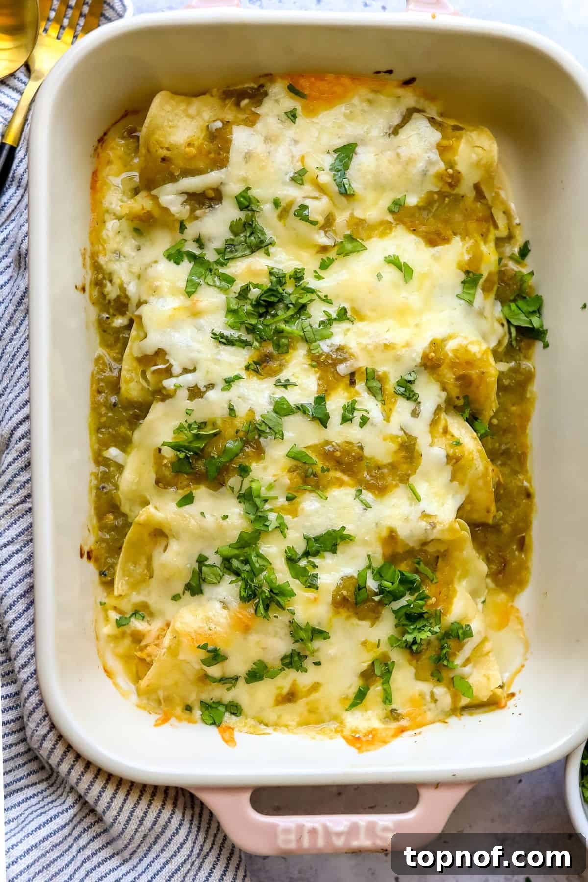 Zesty Green Chile Chicken Enchiladas 5 A close-up view of freshly baked Green Chili Chicken Enchiladas, golden brown and bubbling with melted cheese in a light pink casserole dish.