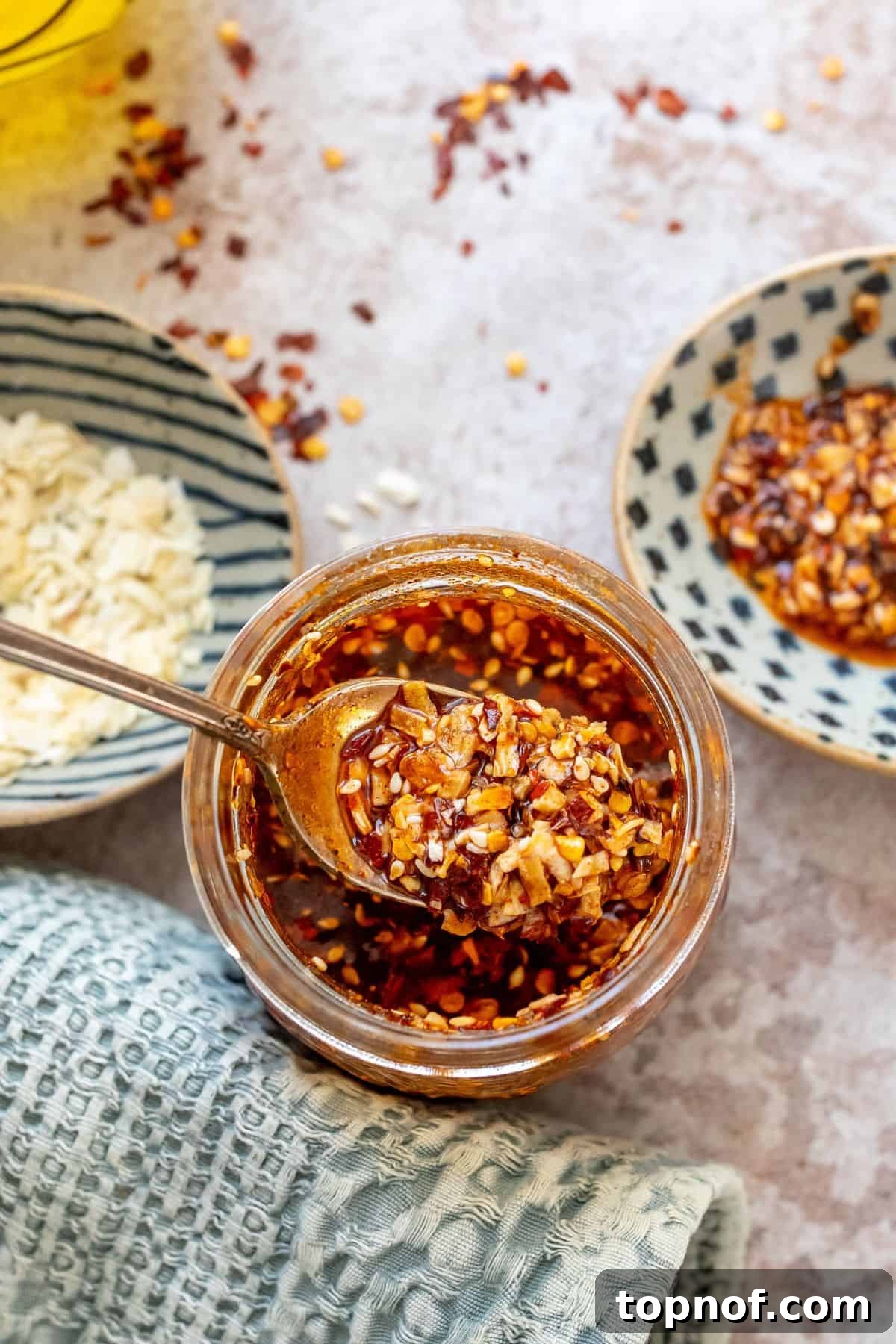 Homemade Trader Joe's Chili Onion Crunch 2 A glass jar filled with homemade Chili Onion Crunch, featuring visible bits of dried garlic and onion, with a silver spoon dipped into it, ready to serve.