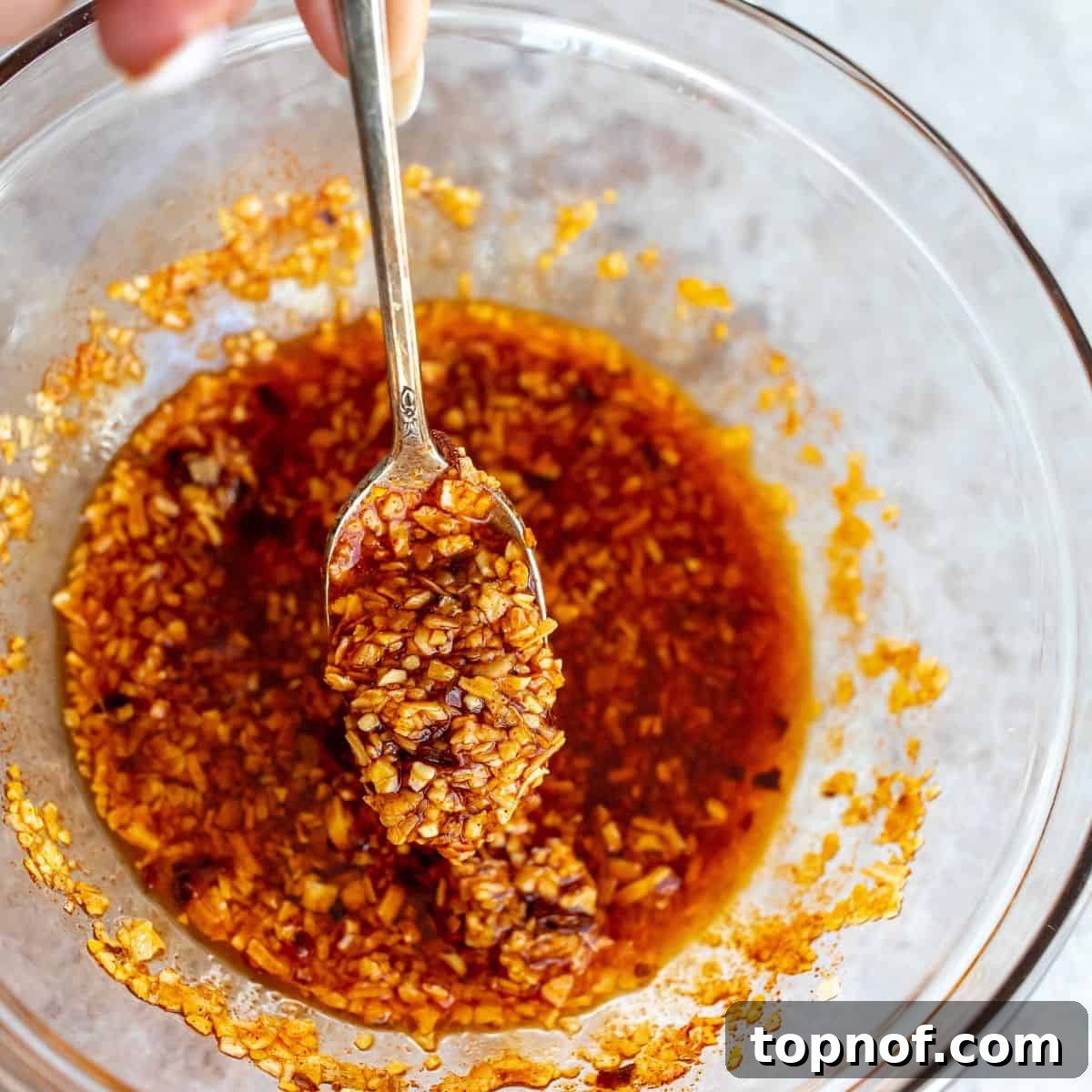 Homemade Trader Joe's Chili Onion Crunch 4 A clear glass bowl filled with the freshly mixed Chili Onion Crunch, showing the vibrant red chili flakes, and dried garlic and onion pieces suspended in oil, with a spoon resting inside the bowl.