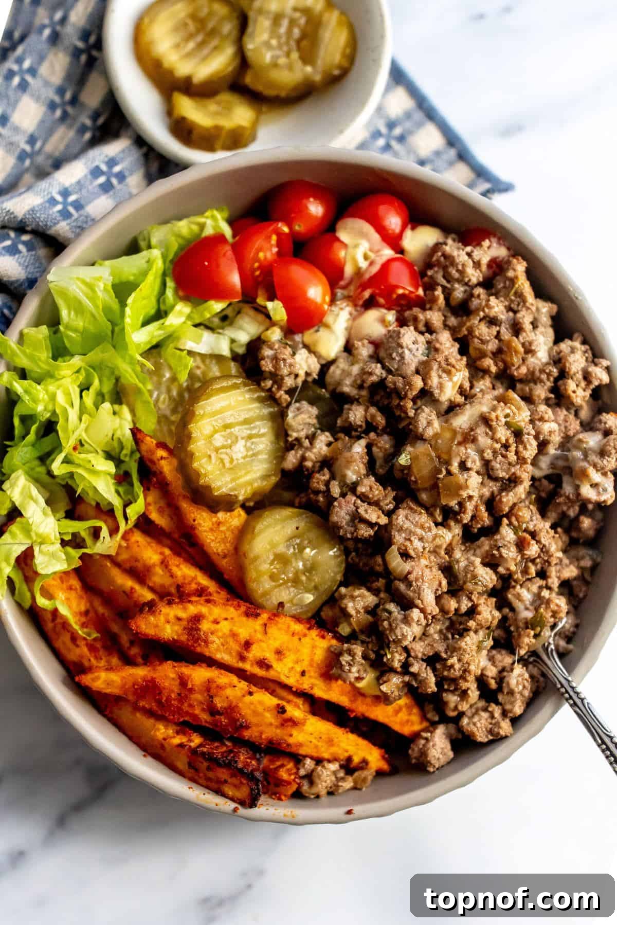 Bunless Cheeseburger Bliss 2 A vibrant cheeseburger bowl brimming with ground beef, melted cheese, crisp lettuce, diced tomatoes, pickles, and a generous drizzle of creamy Big Mac sauce in a modern grey bowl.