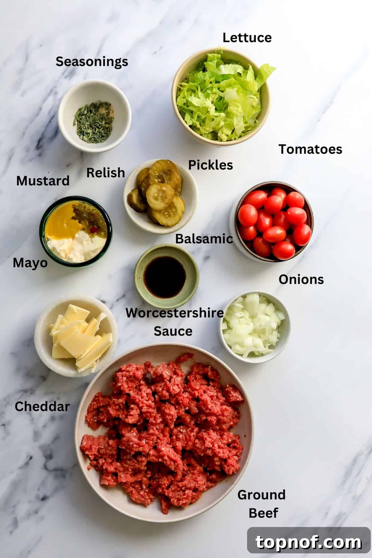 Bunless Cheeseburger Bliss 3 A curated display of fresh ingredients in separate bowls on a grey counter, ready for assembling the cheeseburger bowl recipe. Includes ground meat, chopped onions, shredded cheese, and sauce ingredients.