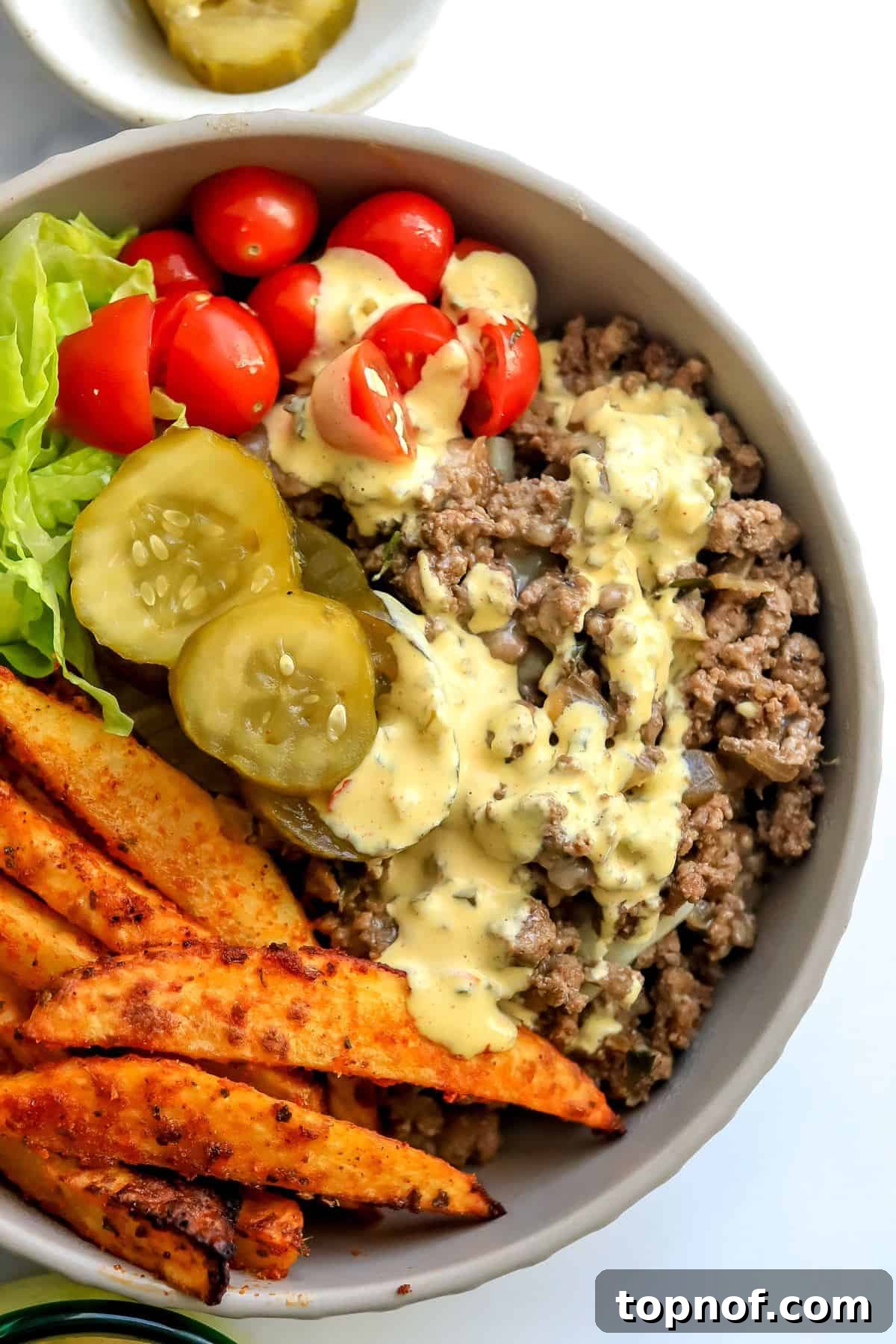 Bunless Cheeseburger Bliss 5 A beautifully assembled ceramic bowl with a cheeseburger base, topped with fresh ingredients and drizzled with creamy sauce, ready to be enjoyed.
