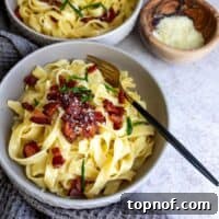 Pasta in a grey bowl with bacon and a fork.