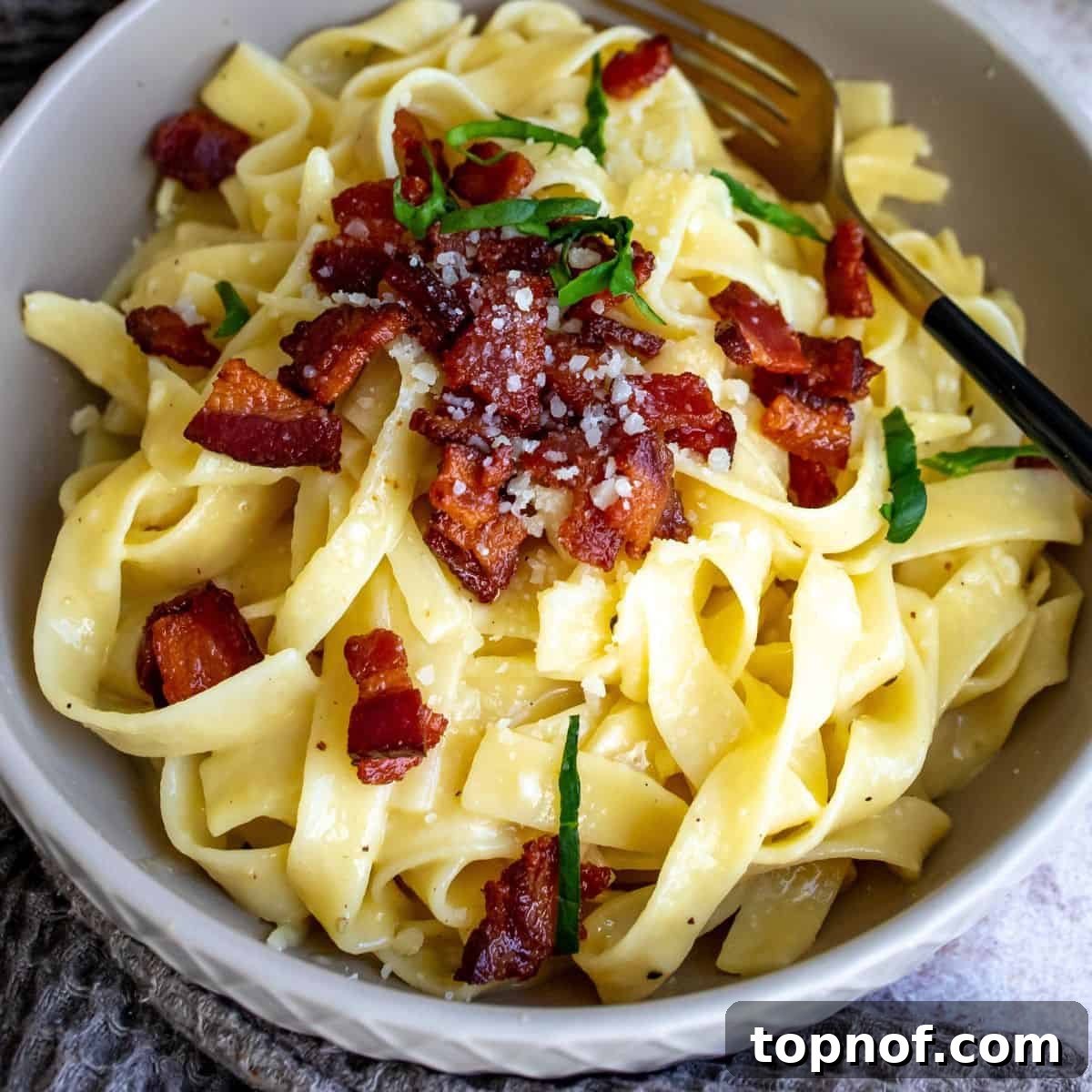 Creamy Carbonara with Crispy Pancetta 6 Close-up of Tagliatelle Carbonara pasta in a grey bowl, topped with crispy pancetta and fresh basil.