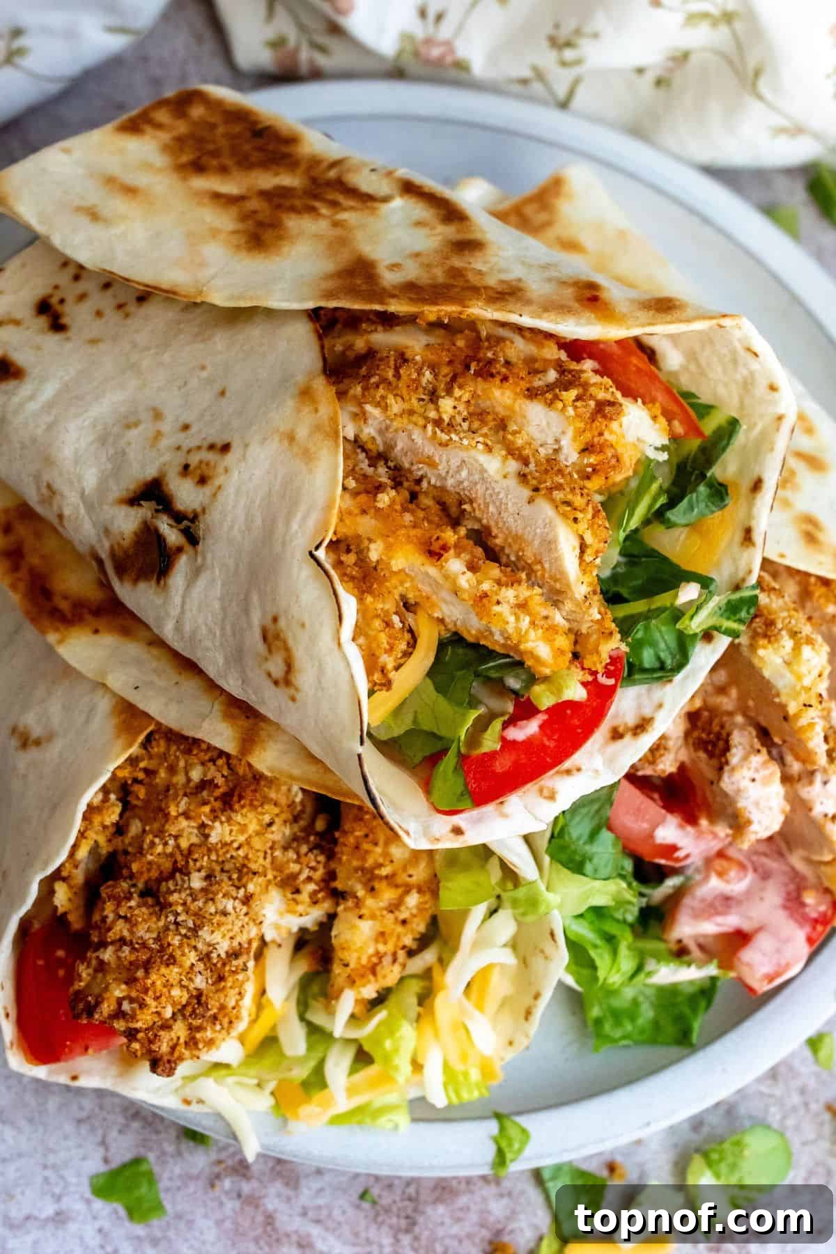 Crispy Chicken Delight 7 A beautifully presented crispy chicken wrap, sliced in half to reveal the delicious layers of chicken, lettuce, tomato, and sauce, arranged on a rustic plate.