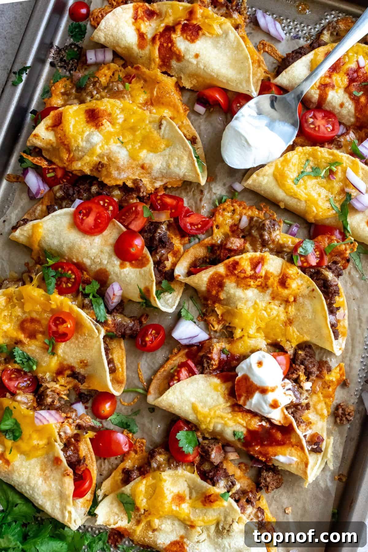 Perfectly Crispy Oven Baked Beef Tacos 2 Crispy beef tacos on a sheet pan with sour cream and fresh cilantro, ready to be served for a delicious taco night.
