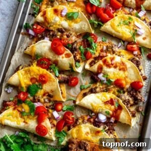 Crispy Beef Tacos on parchment liked baking sheet with hot sauce and tomatoes.