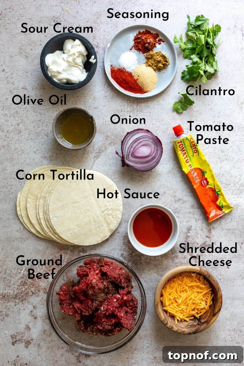 Perfectly Crispy Oven Baked Beef Tacos 3 A collection of fresh ingredients for crispy beef tacos, neatly arranged in clear and wooden bowls on a grey kitchen counter, including ground beef, spices, red onion, and tortillas.