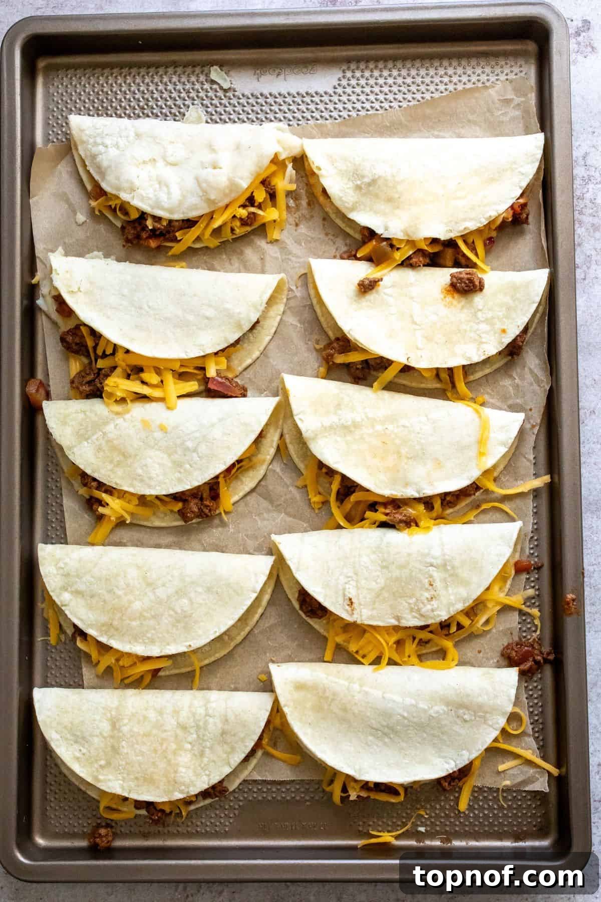 Perfectly Crispy Oven Baked Beef Tacos 5 Multiple crispy beef tacos neatly arranged and folded on a cooking sheet lined with parchment paper, ready for baking to golden perfection.
