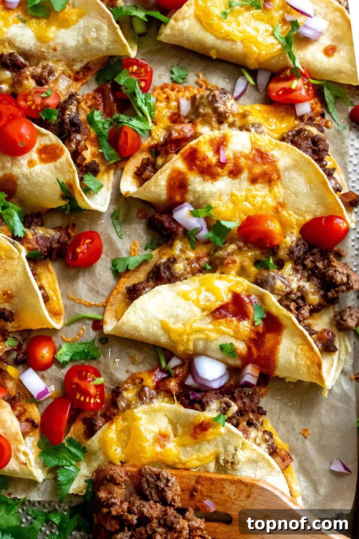 Perfectly Crispy Oven Baked Beef Tacos 6 Five crispy beef tacos, beautifully golden-brown and filled, presented on a parchment-lined baking sheet alongside fresh hot sauce and chopped tomatoes, ready to be devoured.