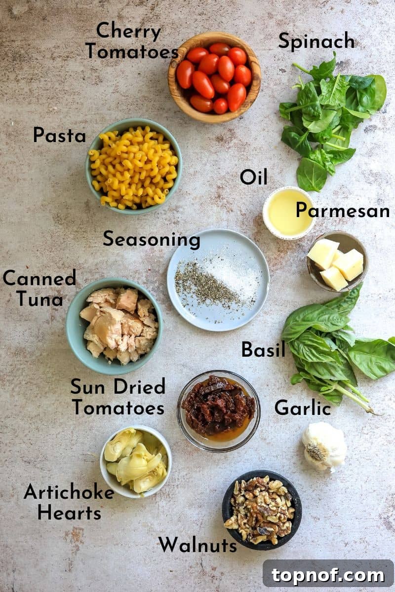 Mediterranean Tuna Pesto Pasta 3 A beautiful flat lay photograph showcasing all the fresh and canned ingredients meticulously laid out on a kitchen counter for making tuna pesto pasta. Small bowls hold vibrant cherry tomatoes, chopped artichoke hearts, and aromatic pesto, alongside a can of tuna and dry pasta.