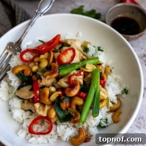 A close-up of Thai cashew chicken, richly sauced and garnished with toasted cashews, served on a white plate.