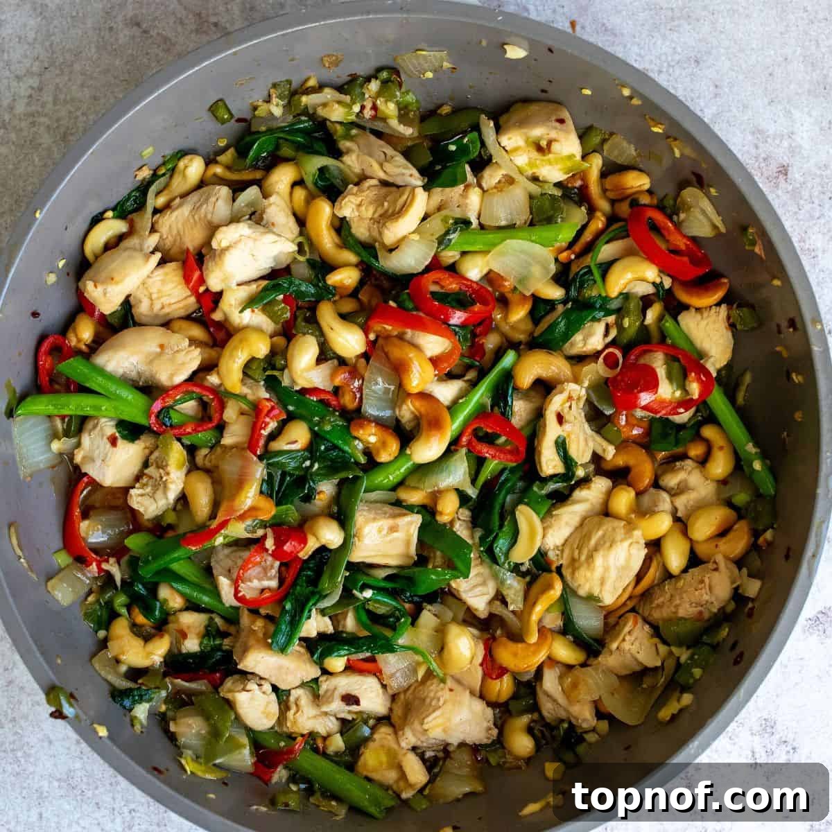 Classic Thai Cashew Chicken 6 A close-up view of succulent chicken pieces and colorful vegetables glistening in a rich, dark sauce within a grey skillet, showcasing the vibrant textures of the dish.