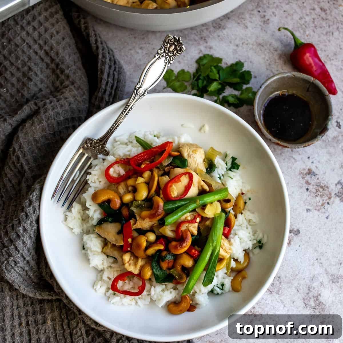 Classic Thai Cashew Chicken 7 A beautifully plated serving of Thai cashew chicken over white rice on a white ceramic plate, adorned with a silver fork, highlighting the rich colors and textures of the meal.