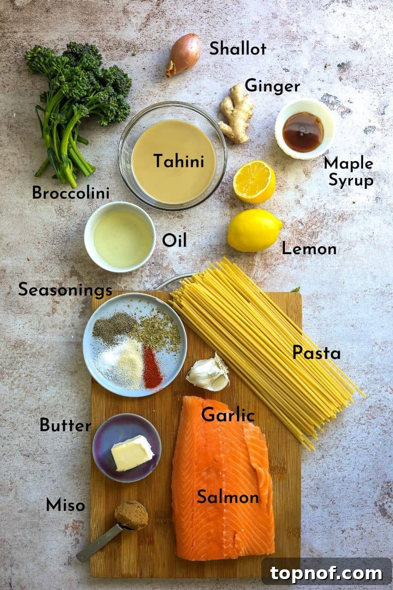 Mediterranean Salmon Tahini Pasta 3 Various fresh ingredients laid out on a kitchen counter, including salmon fillets, broccolini, tahini, ginger, garlic, lemon, and miso paste, ready for preparation.