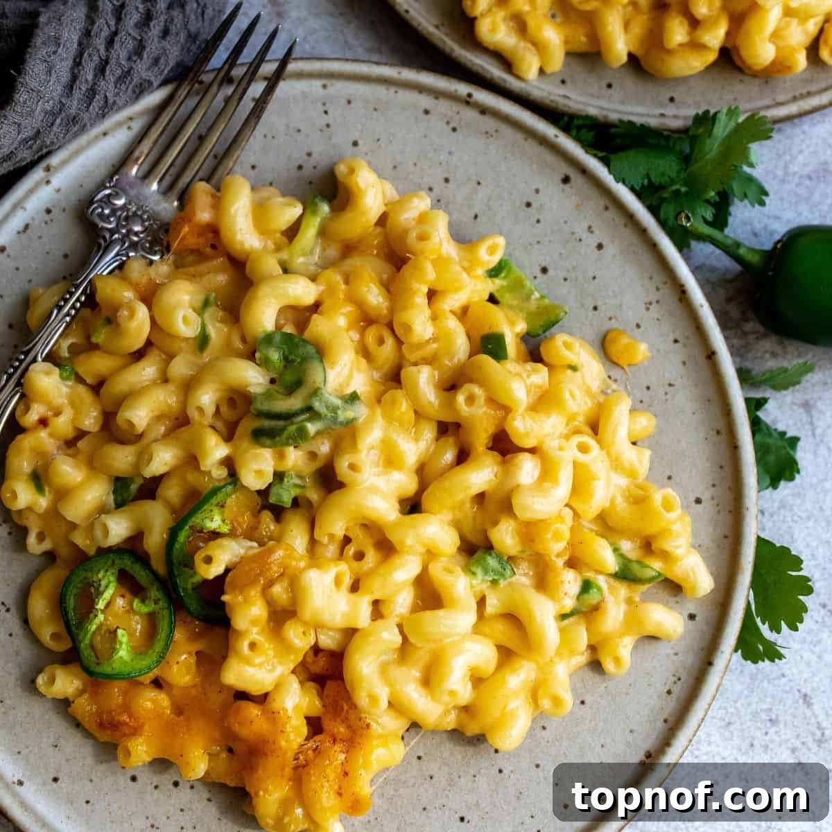 Fiery Mac & Cheese 2 Cheesy pasta with jalapeños and spice on a plate, garnished with fresh herbs.