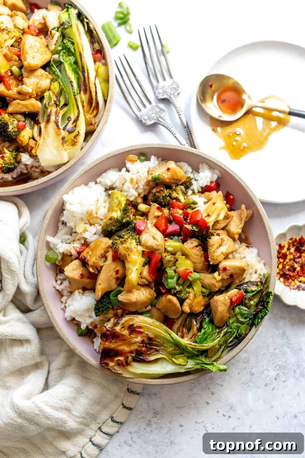 Glazed Teriyaki Chicken Power Bowl 2 Delicious Teriyaki Chicken Rice Bowls, ready to serve on a rustic counter with a plate and spoon nearby.