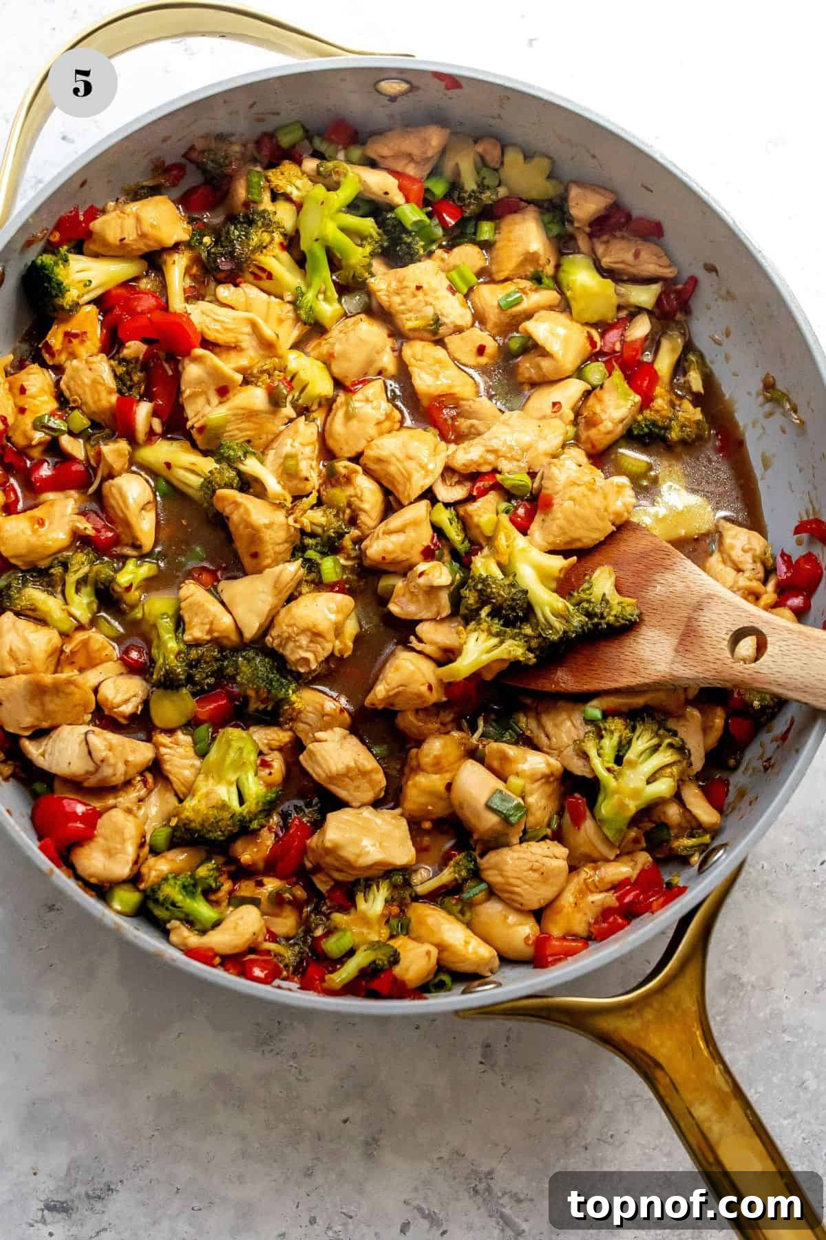 Glazed Teriyaki Chicken Power Bowl 5 A grey skillet filled with perfectly cooked teriyaki chicken and vegetables, with a wooden spoon resting inside.