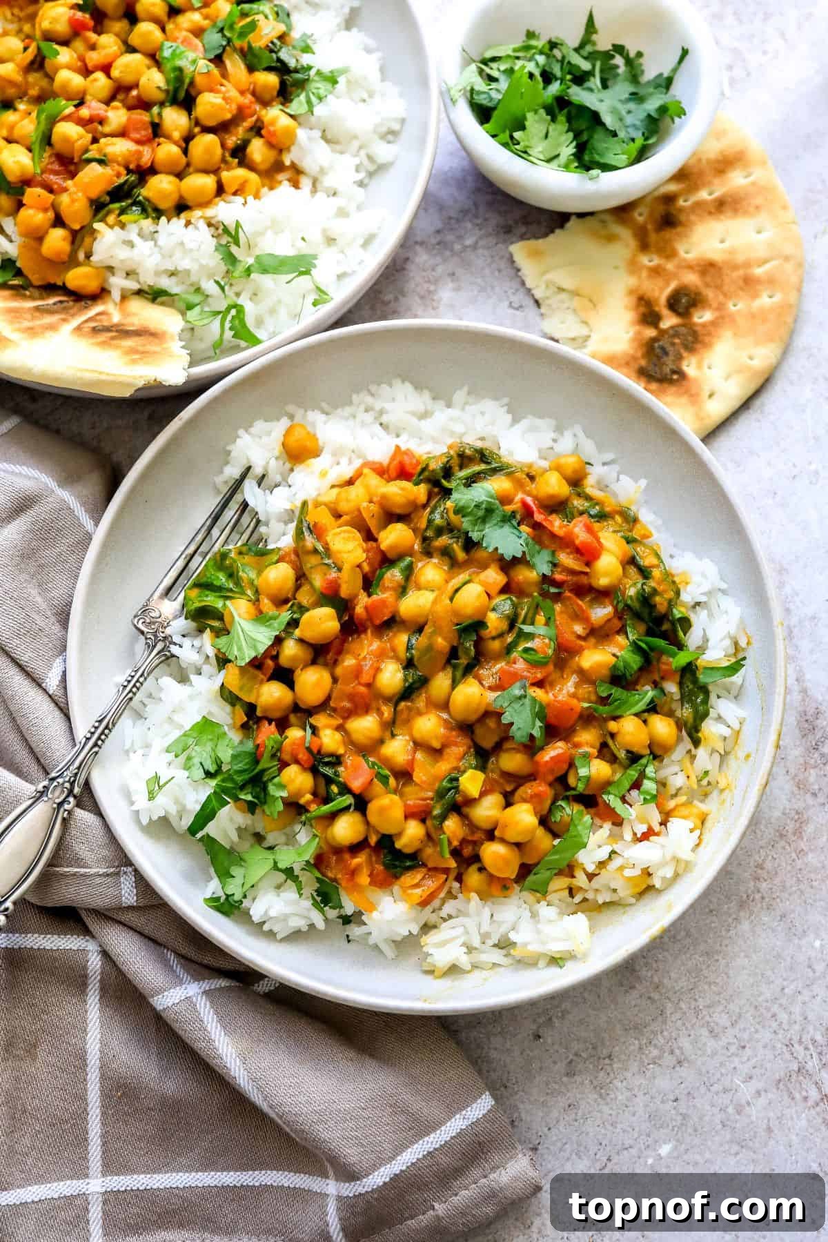 Vibrant Chickpea and Spinach Curry 2 Two white ceramic bowls filled with Chickpea Spinach Curry and fluffy white rice, placed next to a silver fork on a light surface.