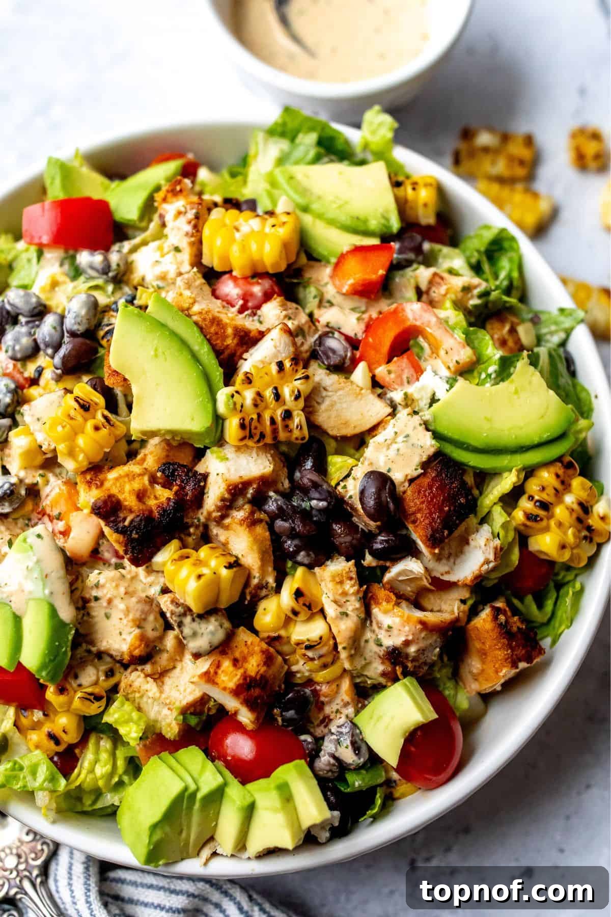 The finished Spicy Southwest Salad, beautifully presented in a white bowl on a clean counter, complete with the rich dressing and juicy chicken.