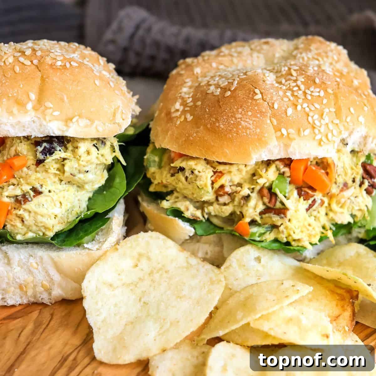 Spiced Chicken Salad 6 Curried chicken salad sandwiches on sesame buns served on a wooden cutting board with a side of chips.