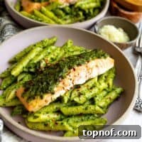 Zesty Salmon Pesto Pasta 7 A close-up of pesto pasta with a salmon fillet on top, garnished with fresh parmesan, showcasing a rich and flavorful meal.