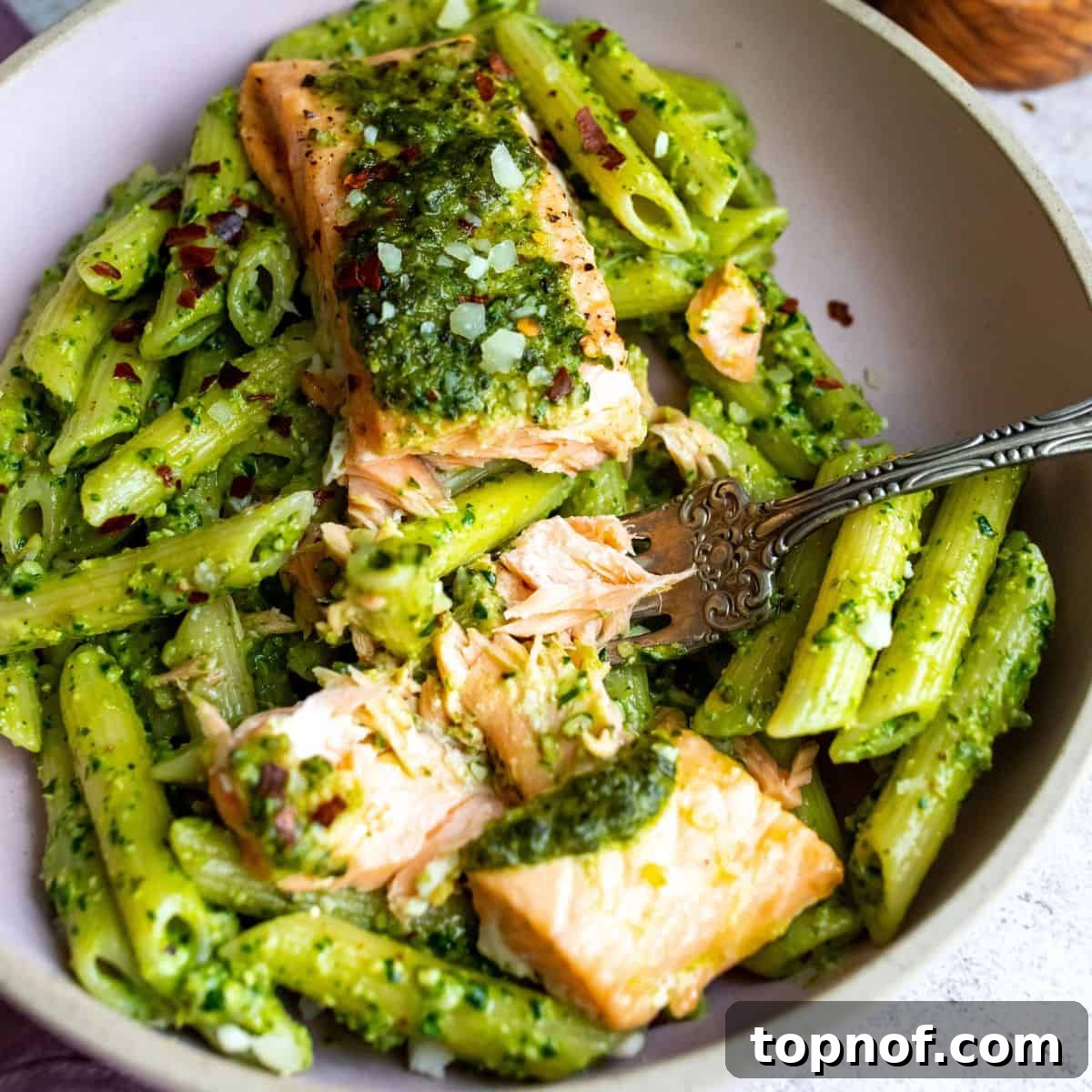 Zesty Salmon Pesto Pasta 6 A close-up of a beautifully plated serving of salmon pesto pasta, featuring tender salmon over vibrant green pesto-coated pasta, with a silver fork resting on the side, ready to be enjoyed.