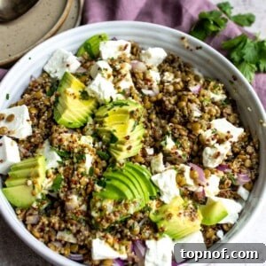 White bowl with a vibrant quinoa lentil salad, garnished with crumbled feta and fresh herbs.