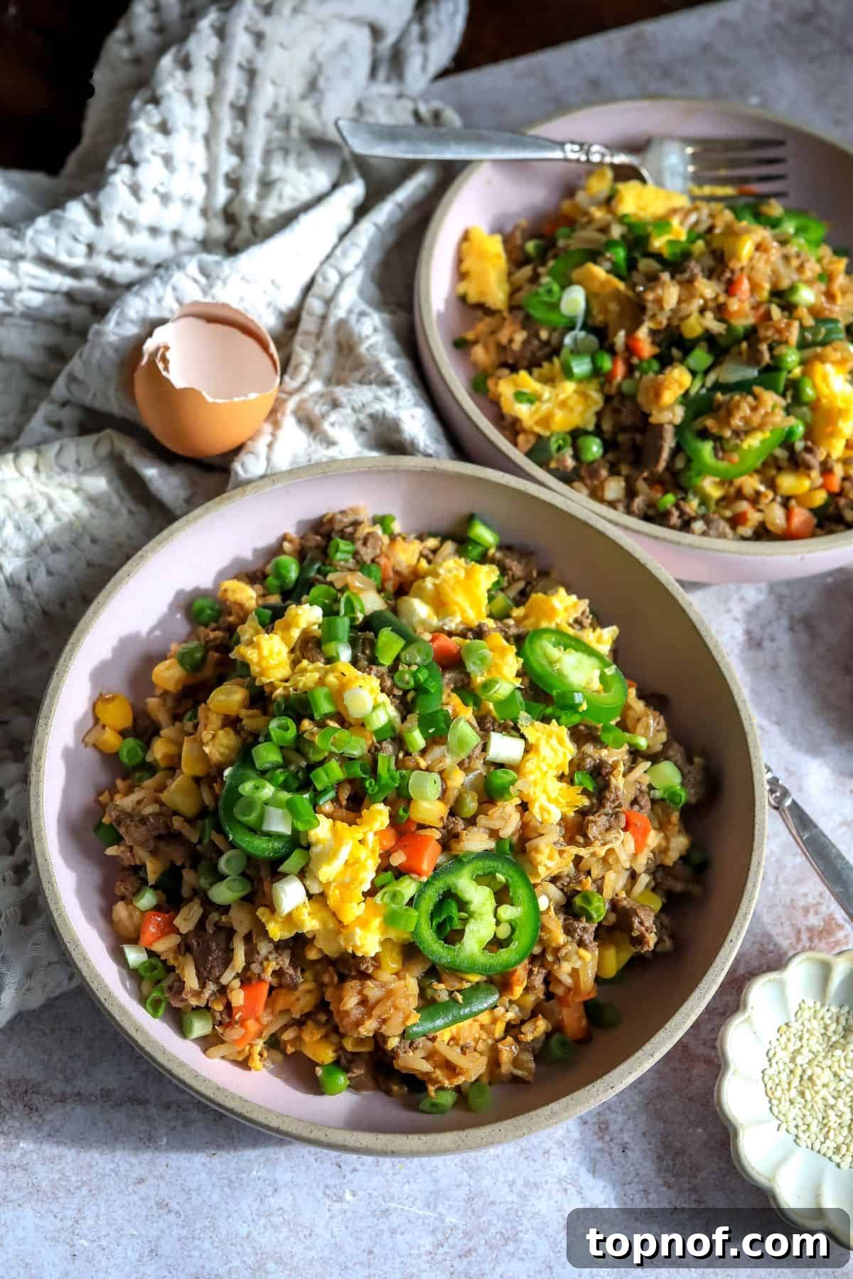 Sizzling Beef Fried Rice 2 Pink bowl with ground beef fried rice in it and topped with green onions.