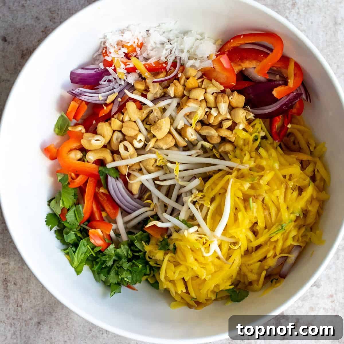 A large white bowl brimming with the colorful ingredients of Thai Mango Salad before tossing, showcasing the fresh mango, vegetables, and herbs.