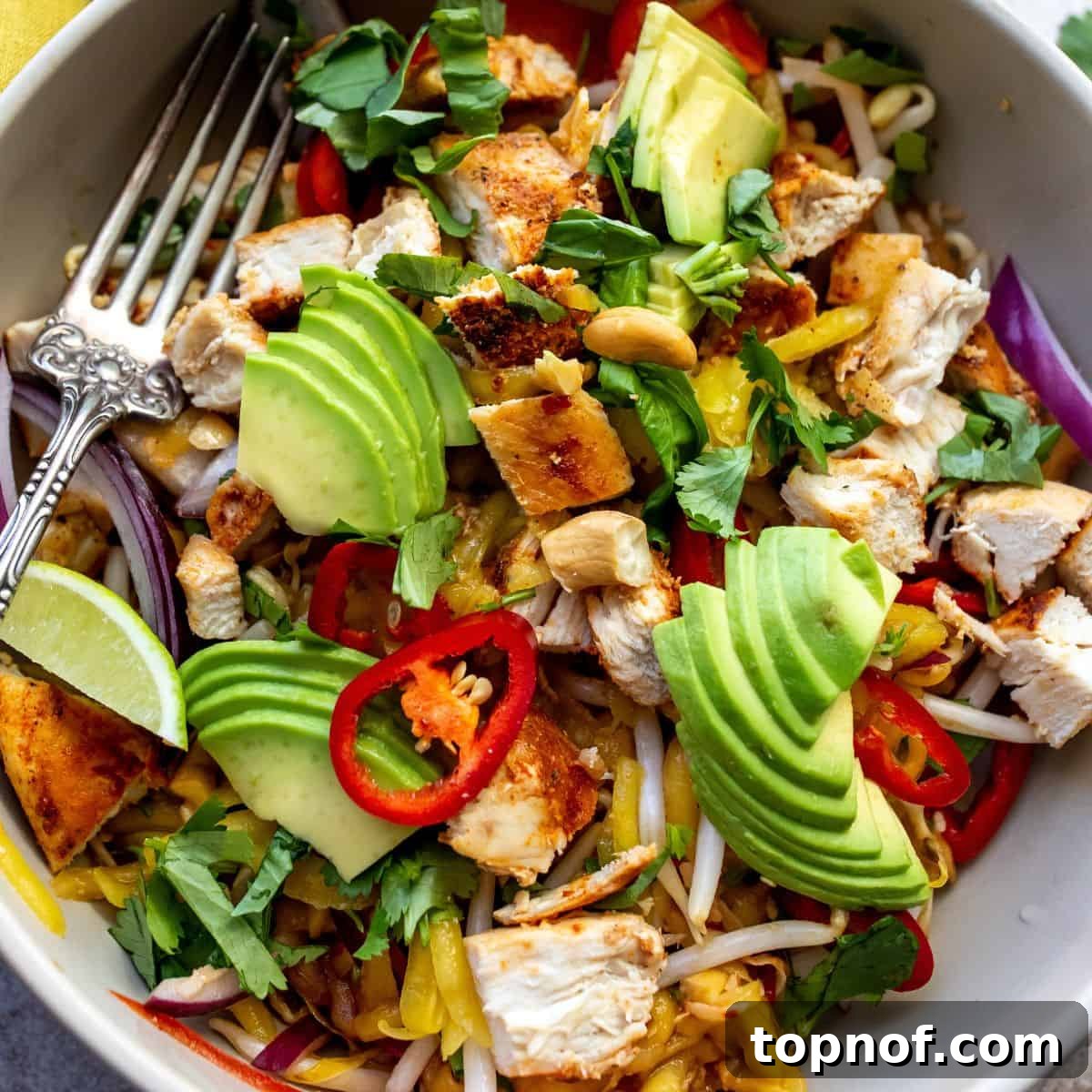A close-up view of a single white bowl filled with finished Thai Mango Salad, highlighting the vibrant colors and textures of the dish.