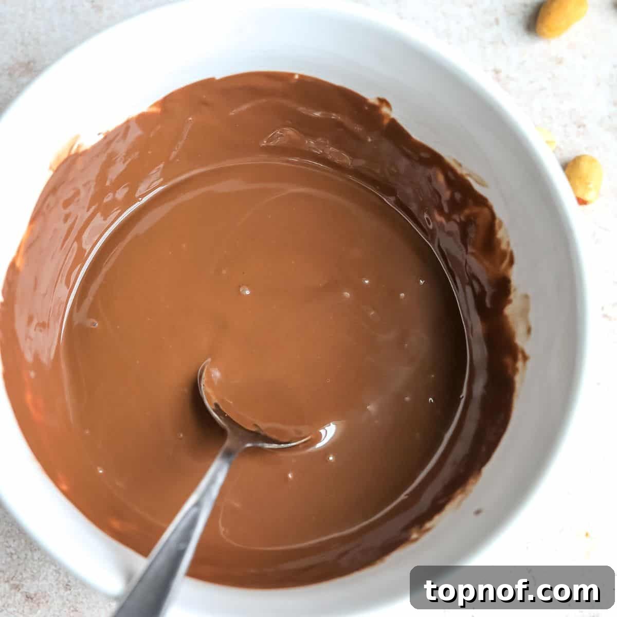 Wholesome Peanut Butter Chocolate Bars 5 A white bowl filled with perfectly melted chocolate and a spoon, ready for the next step of the buckeye bar recipe.