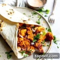 Tortilla with chicken inside with lettuce and a fork on a plate.