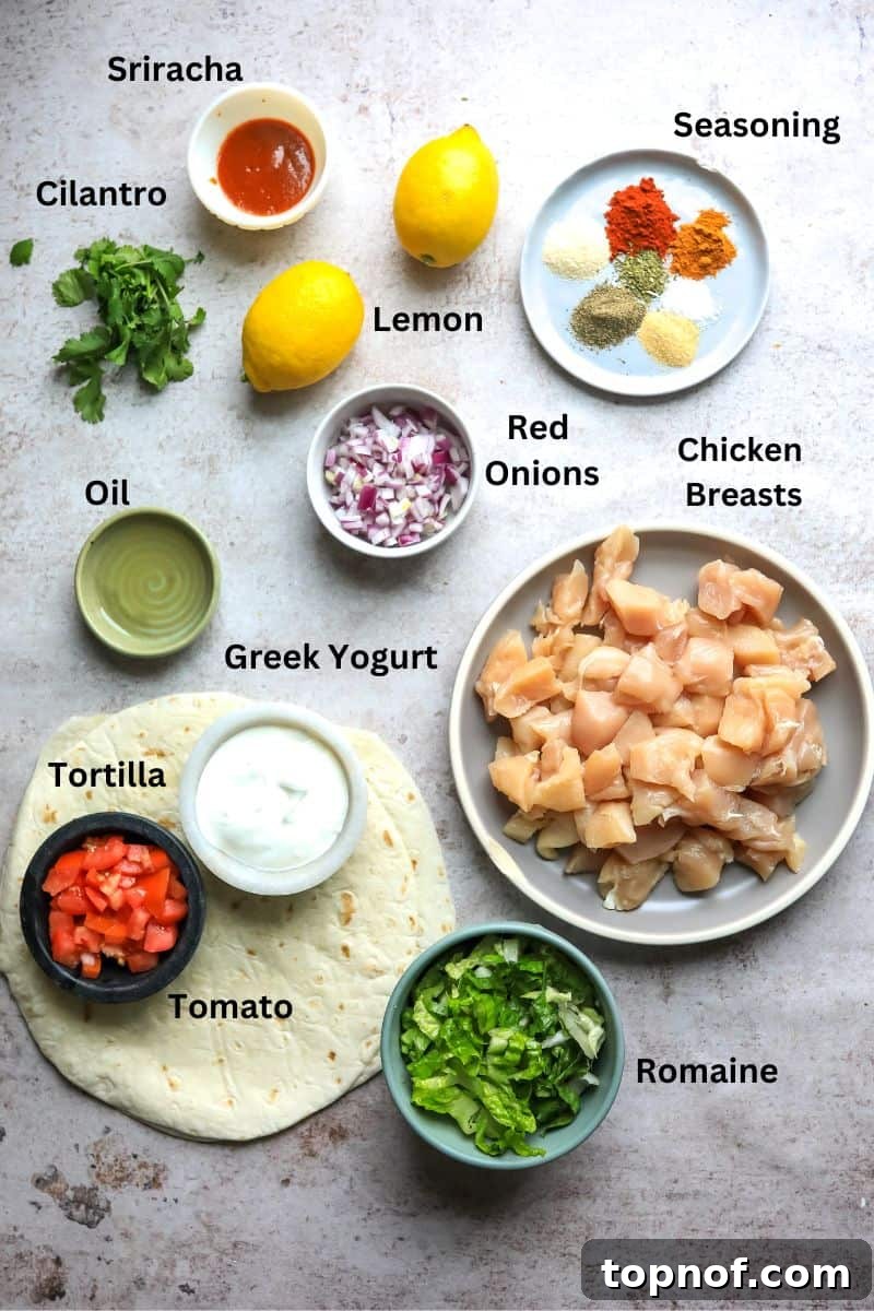 Various fresh ingredients laid out on a kitchen counter, including chicken breasts, spices, olive oil, lemon, Greek yogurt, Sriracha, red onion, tomatoes, and cilantro.