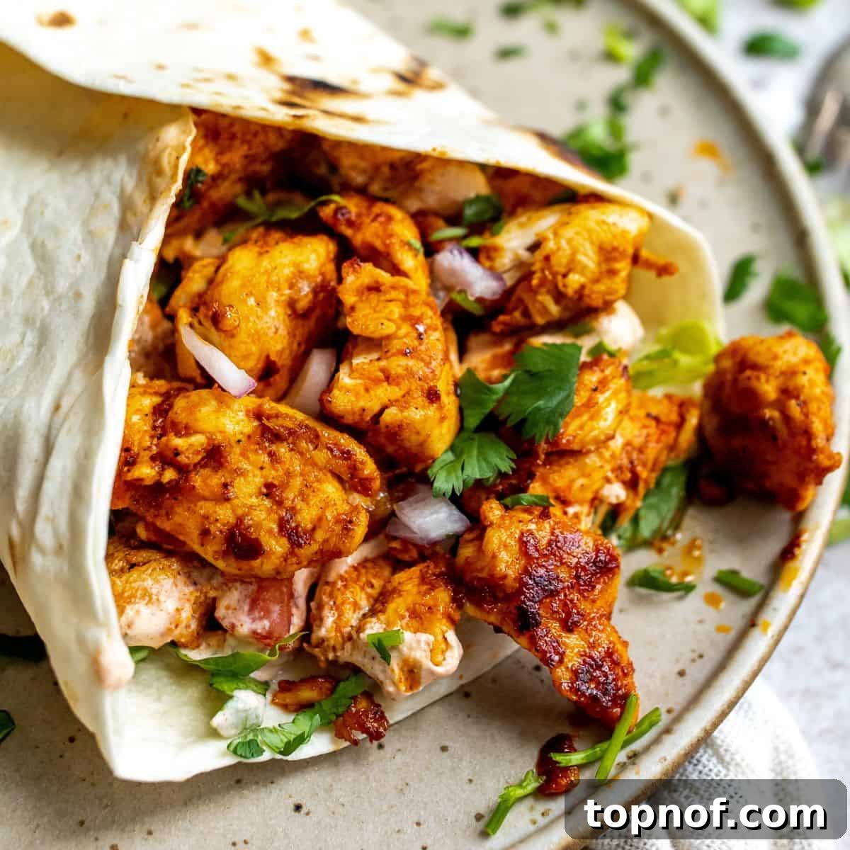 A finished spicy Cajun chicken wrap, neatly folded and placed on a pristine white plate, garnished with fresh cilantro.