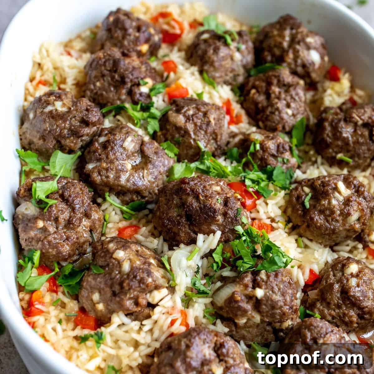 Comforting Meatball and Rice Bowl 7 Close-up shot of juicy venison meatballs nestled in flavorful rice, served in a white casserole dish, garnished with fresh herbs.