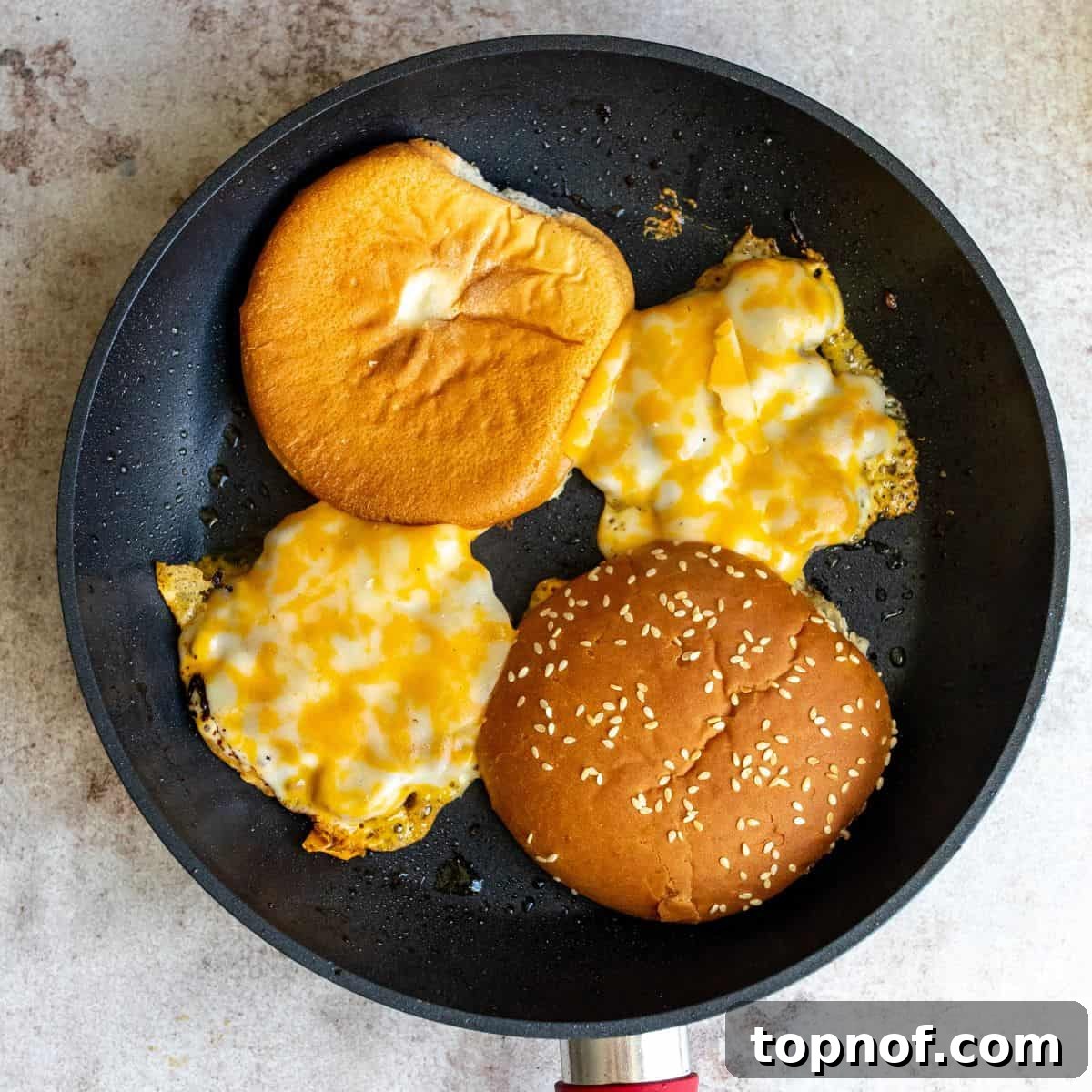 Signature Turkey Smash Burgers 6 Cheesy turkey smash burgers and toasted sesame buns cooking on a Blackstone or frying pan.