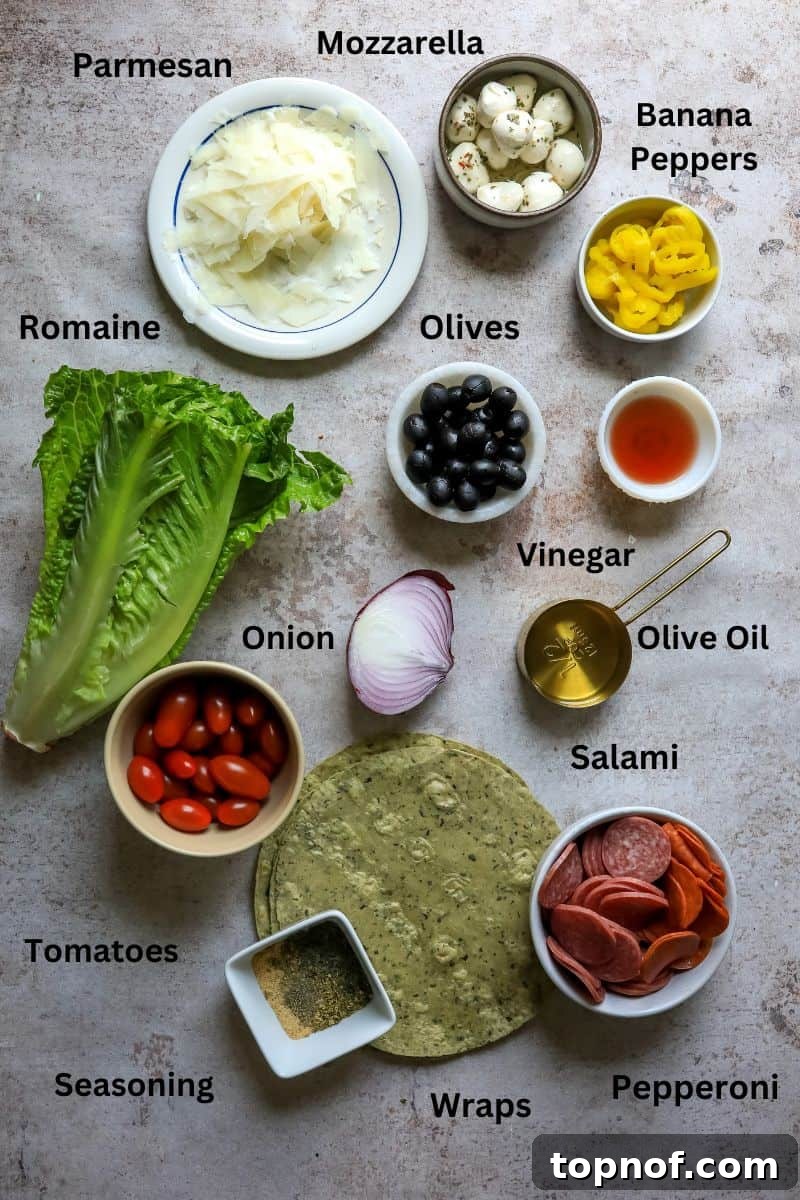 Tuscan Pinwheels 3 A vibrant selection of fresh ingredients including salami, pepperoni, romaine lettuce, cherry tomatoes, red onion, black olives, peperoncini, parmesan, and mozzarella cheese on a kitchen counter, ready for making Italian wraps.