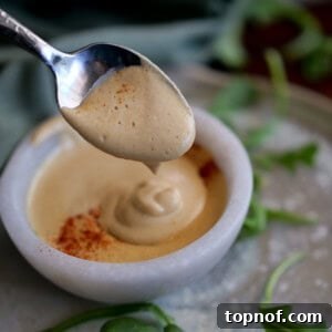 A vibrant bowl of Easy Vegan White Cheddar Sauce with a spoon, garnished with fresh herbs.