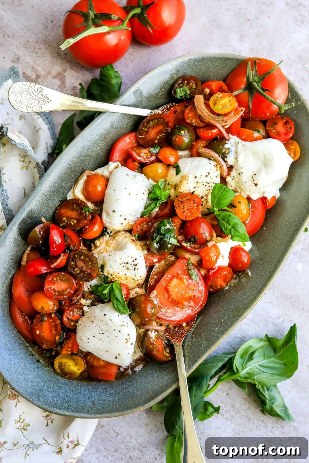 Creamy Burrata Tomato Bliss 2 Green serving dish with vibrant red and yellow tomatoes, creamy white burrata cheese, and fresh green basil leaves. The dish is generously seasoned and drizzled with dressing.